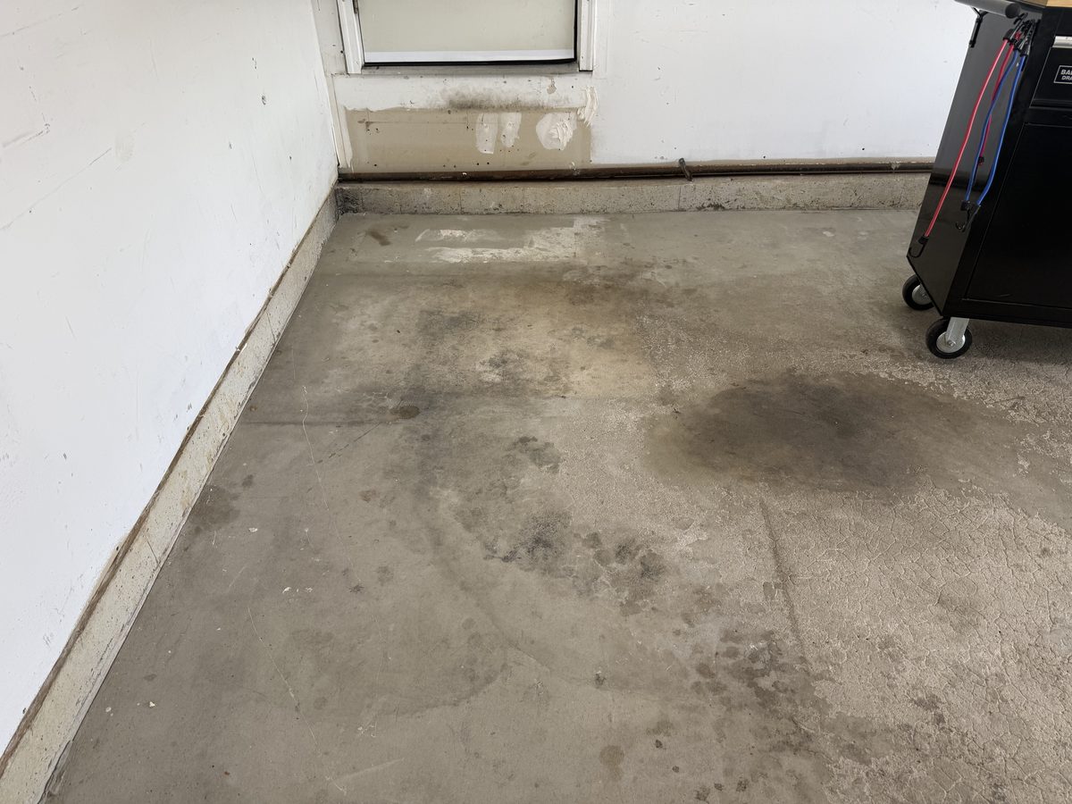 Garage interior before coating — bare, stained concrete under stored clutter